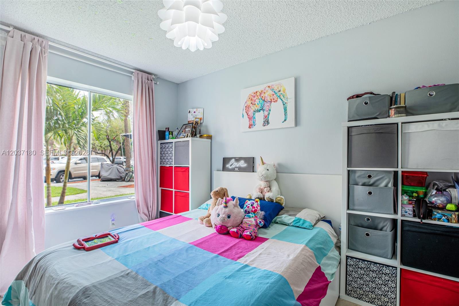 A bedroom features a bed with a colorful quilt, storage cubbies, and a window view — 15780 SW 106th Ter # 107, Miami FL 33196, MIAMI, FL