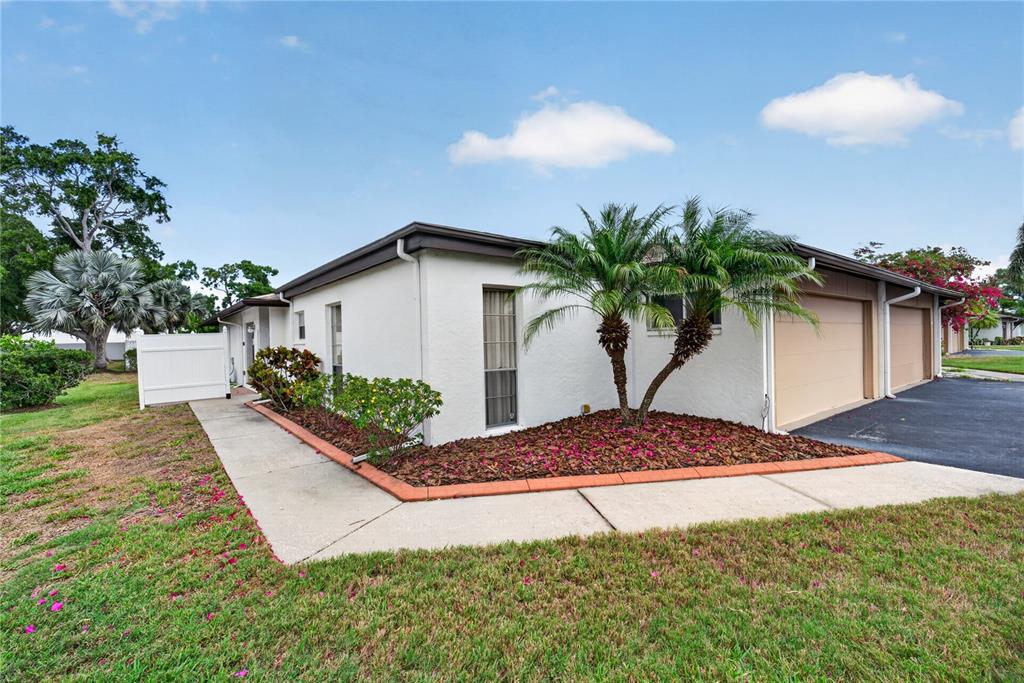 A single-story white stucco building features a palm tree, a small garden, and garage doors — 3501 N VILLAGE COURT UNIT 220, SARASOTA, FL