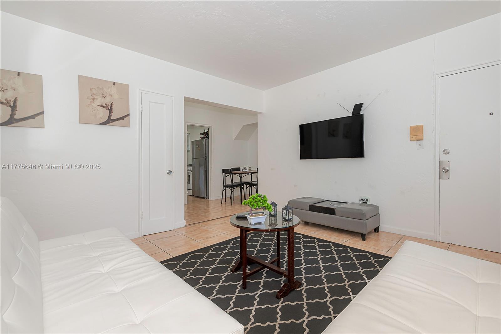 A living room features white sofas, a patterned rug, a glass coffee table, and a wall-mounted television — 655 83rd St # 55, Miami Beach FL 33141, MIAMI BEACH, FL