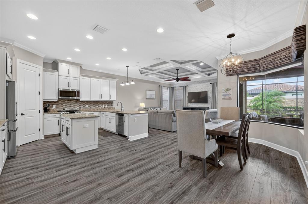 An open-concept kitchen and dining area features white cabinetry, granite countertops, and wood-look flooring — 5010 TIVOLI RUN, BRADENTON, FL