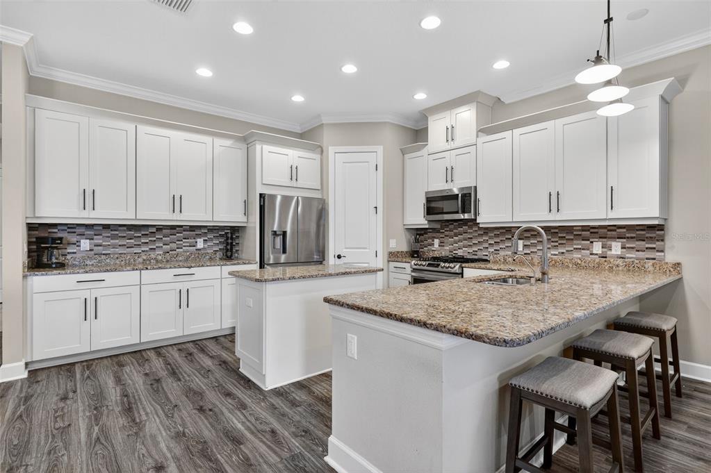 A kitchen features white cabinets, granite countertops, a tiled backsplash, and a central island — 5010 TIVOLI RUN, BRADENTON, FL