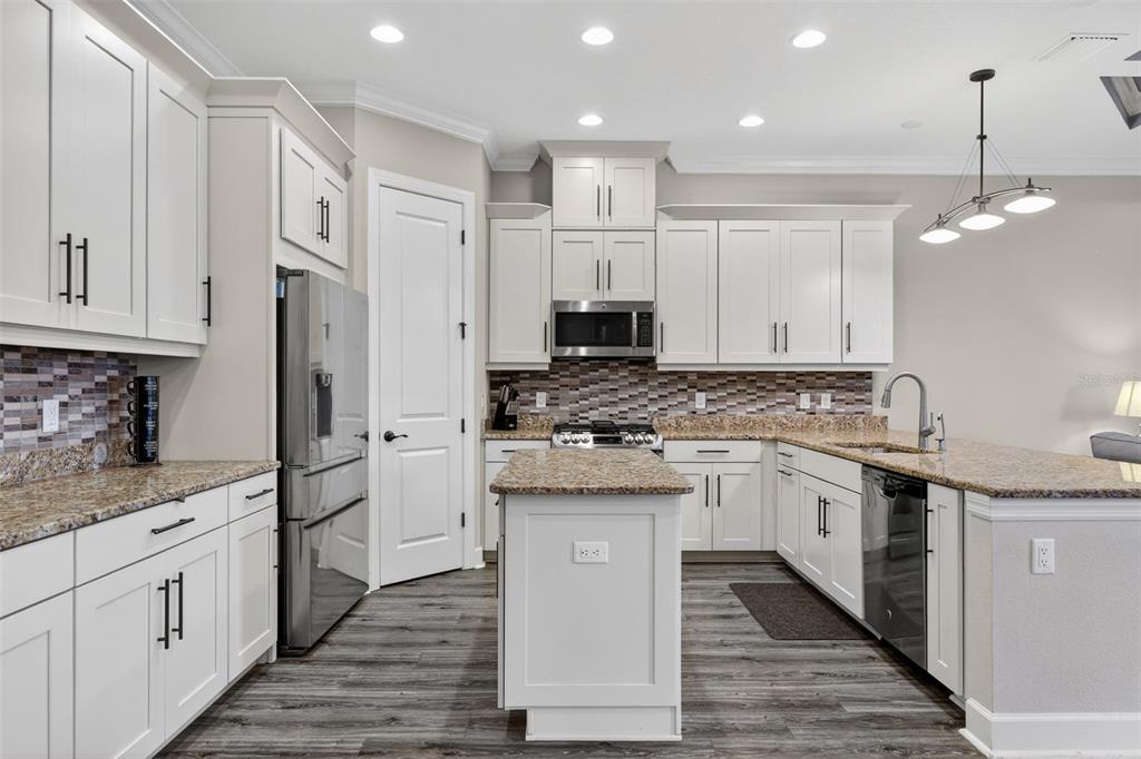 A kitchen features white cabinetry, granite countertops, stainless steel appliances, and wood-look flooring — 5010 TIVOLI RUN, BRADENTON, FL