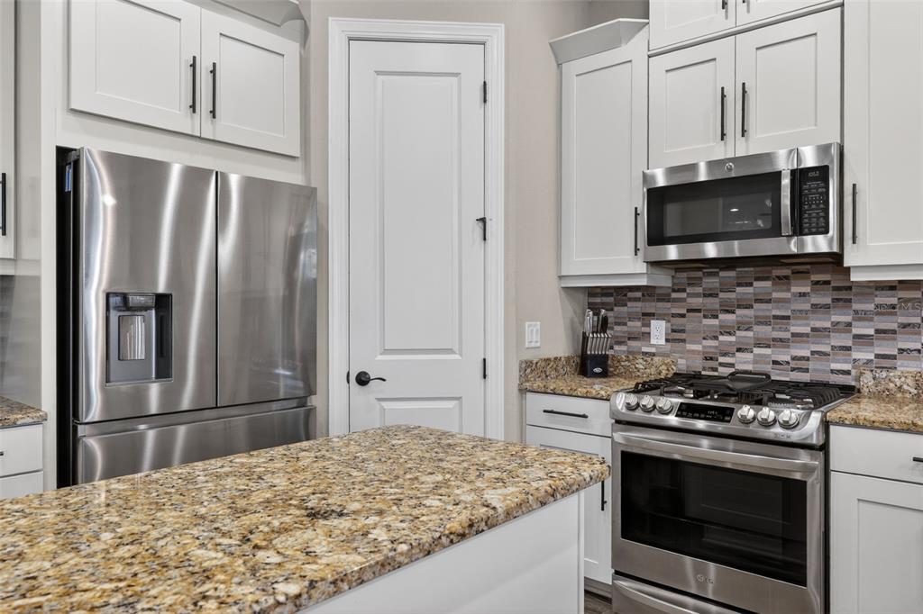A kitchen features white cabinets, stainless steel appliances, granite countertops, and a mosaic tile backsplash — 5010 TIVOLI RUN, BRADENTON, FL