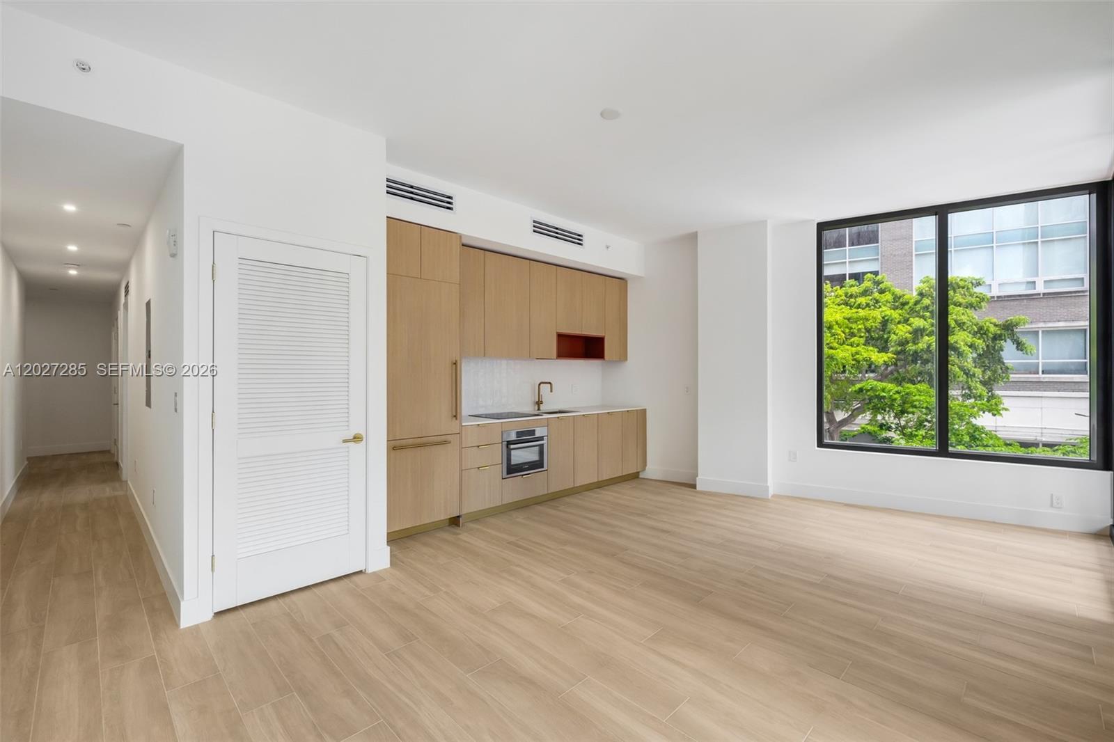 A modern kitchen with light wood cabinetry and a large window overlooking green trees — 90 NE 32nd St # 212, Miami FL 33127, MIAMI, FL