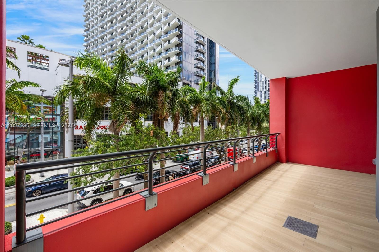 A balcony with red walls, a metal railing, and light-colored tile flooring overlooks a city street — 90 NE 32nd St # 212, Miami FL 33127, MIAMI, FL