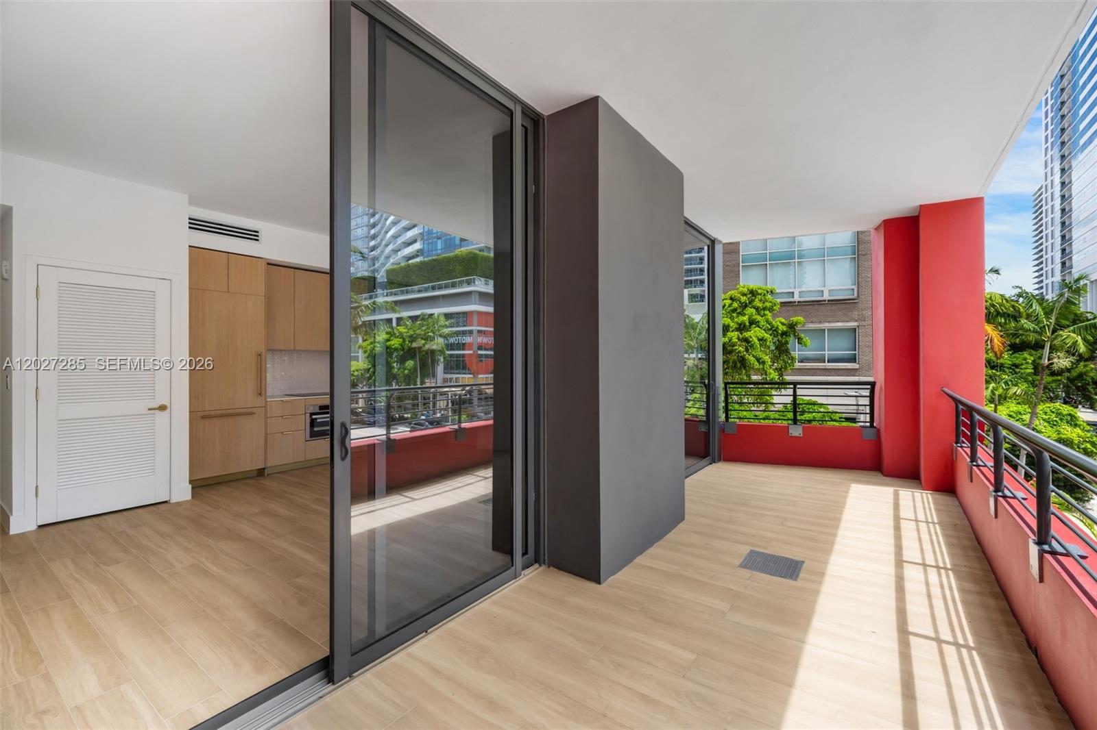 A balcony with light wood-look flooring and red walls overlooks an urban street scene — 90 NE 32nd St # 212, Miami FL 33127, MIAMI, FL
