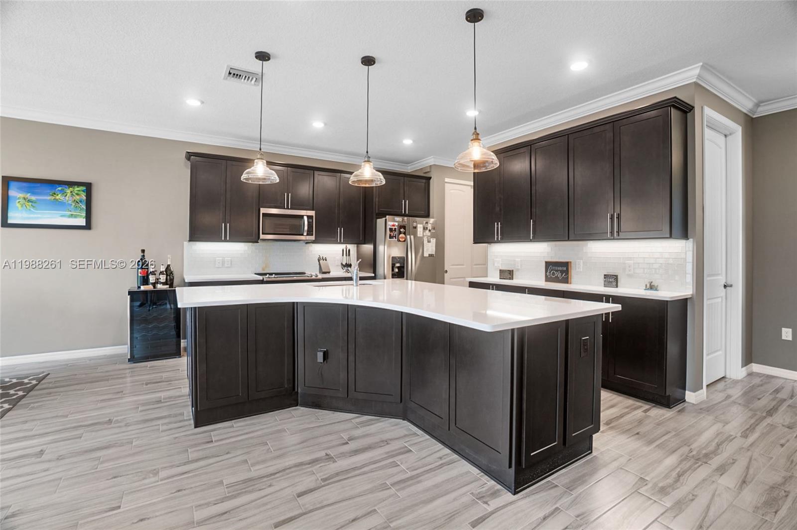 A modern kitchen features dark wood cabinets, white countertops, a large island, and pendant lighting — 8240 Tailshot Ct, Lake Worth FL 33467, LAKE WORTH, FL