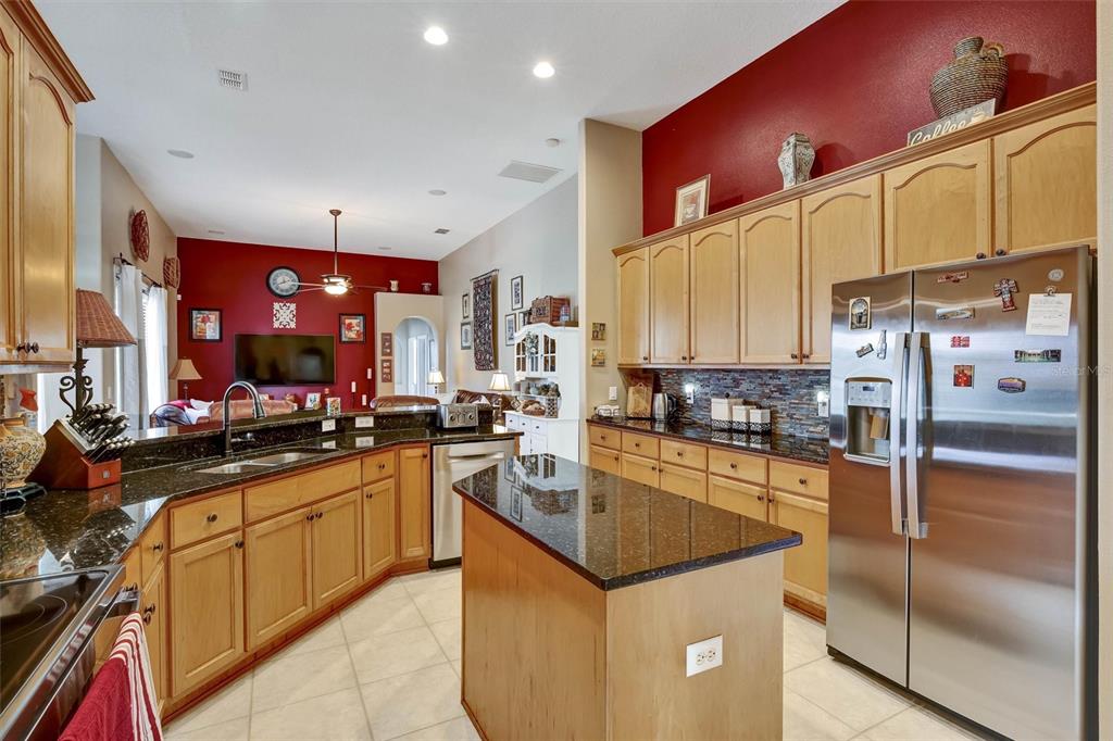 A kitchen features light wood cabinets, dark granite countertops, a center island, and red walls — 1527 GANTS CIRCLE, KISSIMMEE, FL