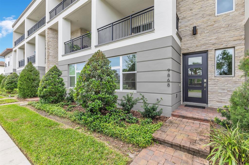 A modern townhouse exterior features a stone facade, gray siding, and a paved entryway — 9868 BUCKLOW HILL DRIVE, ORLANDO, FL