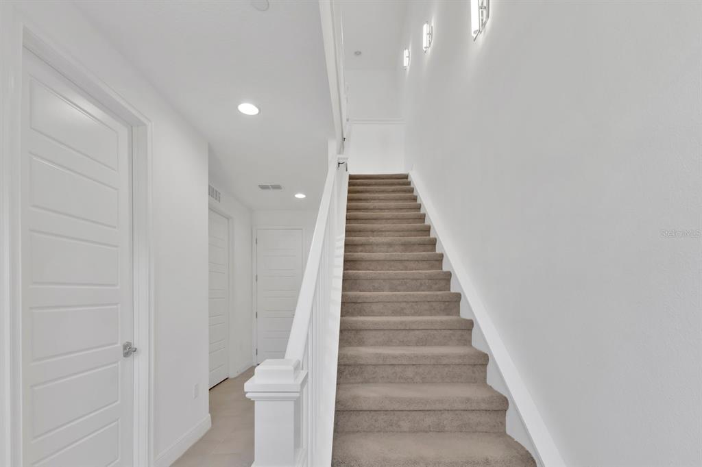 A carpeted staircase with white railings leads upward in a bright, minimalist hallway — 9868 BUCKLOW HILL DRIVE, ORLANDO, FL