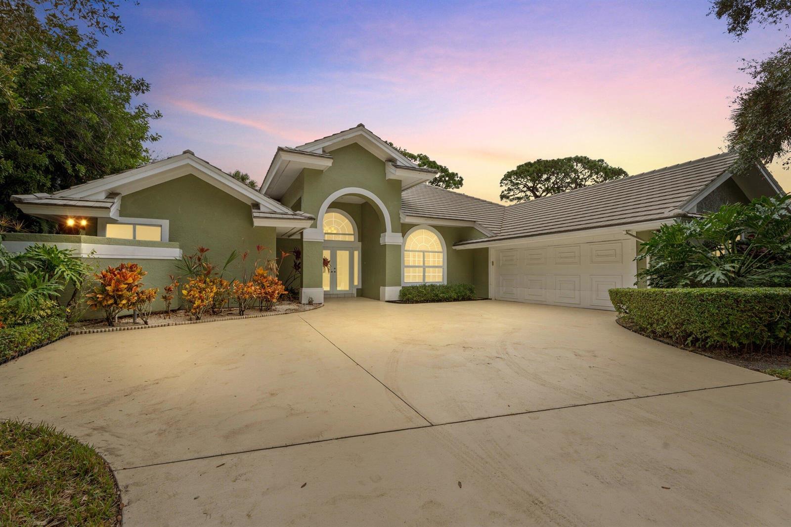 A green single-story house with a tiled roof, arched entryway, and a large concrete driveway — 6581 SE Baltusrol Terrace, Stuart FL 34997, STUART, FL