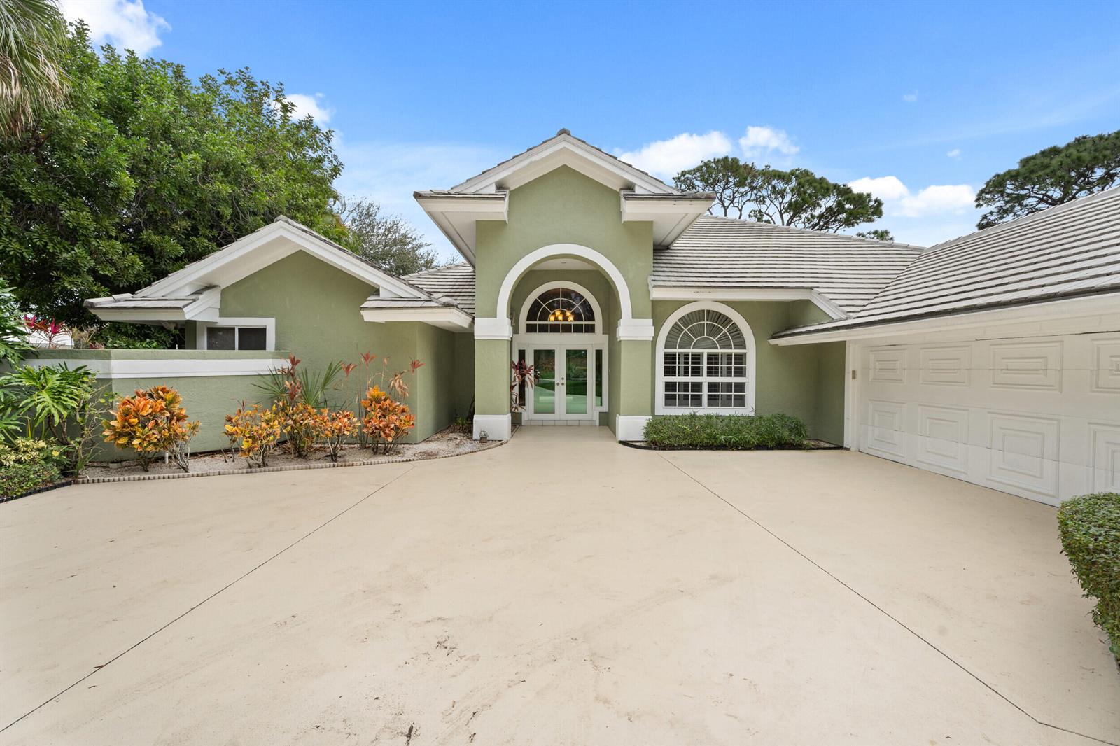 A green single-story house with a large driveway, arched entryway, and white garage door — 6581 SE Baltusrol Terrace, Stuart FL 34997, STUART, FL