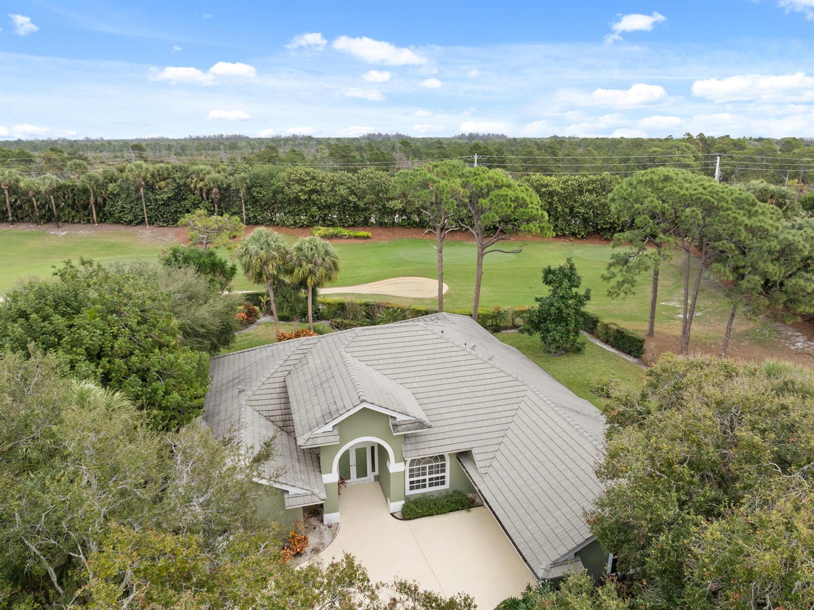 An aerial view shows a green house with a tiled roof situated next to a golf course — 6581 SE Baltusrol Terrace, Stuart FL 34997, STUART, FL
