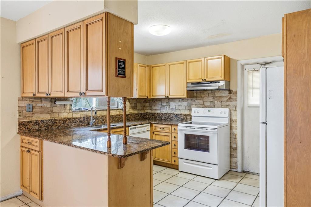 A kitchen features light wood cabinets, granite countertops, a white stove, and a stone backsplash — VERO BEACH, FL