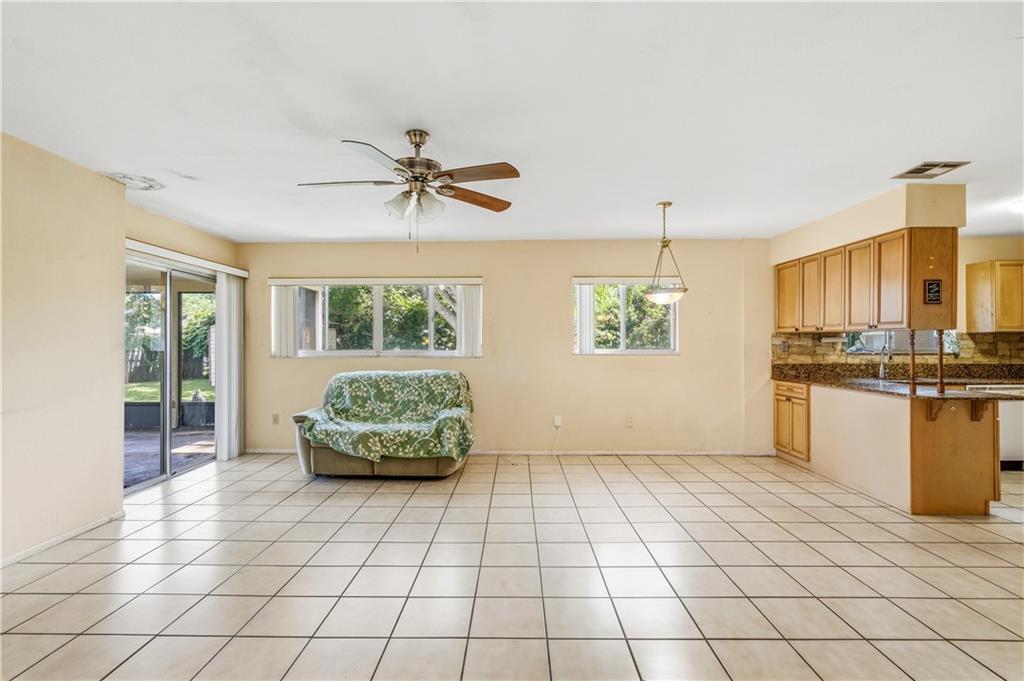 An open-concept room features light-colored tile floors, a ceiling fan, and an adjacent kitchen — VERO BEACH, FL