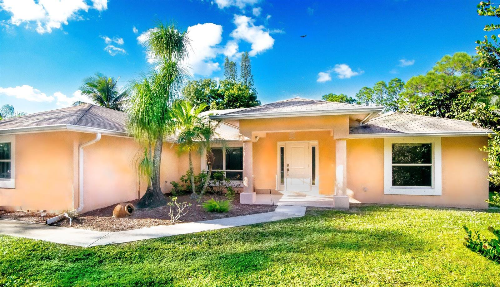A single-story peach-colored house with a white front door and a palm tree in front — 12523 169th Court N, Jupiter FL 33478, JUPITER, FL