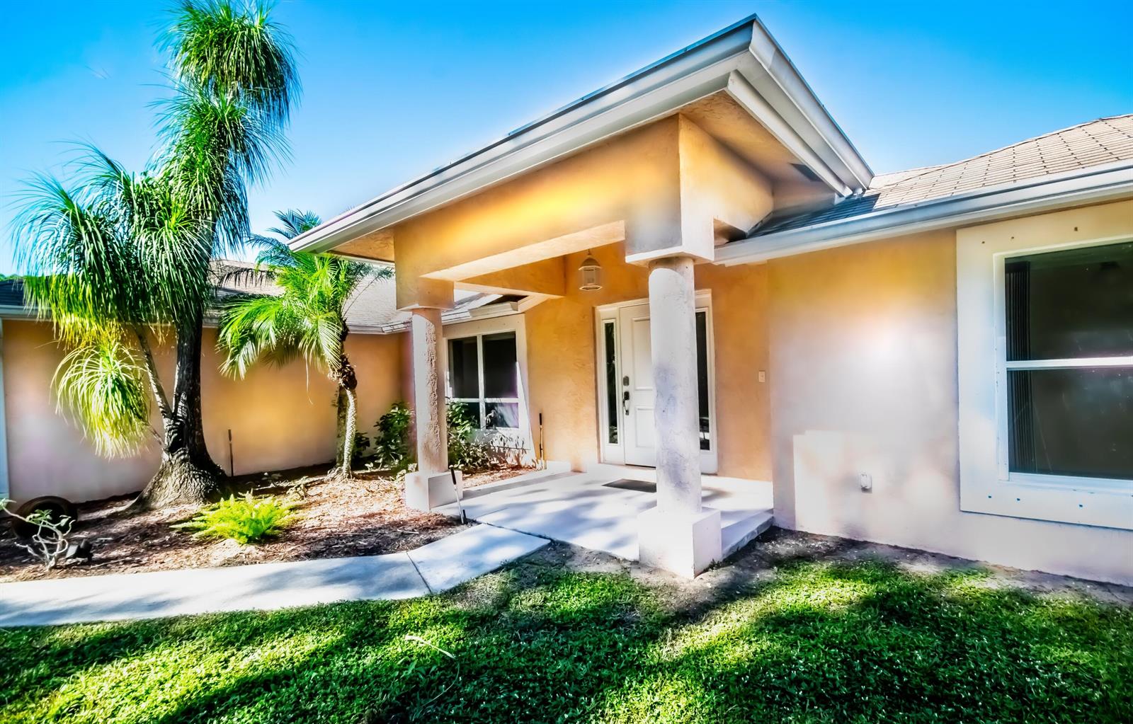 A tan stucco house exterior features a covered entryway with two columns and palm trees — 12523 169th Court N, Jupiter FL 33478, JUPITER, FL