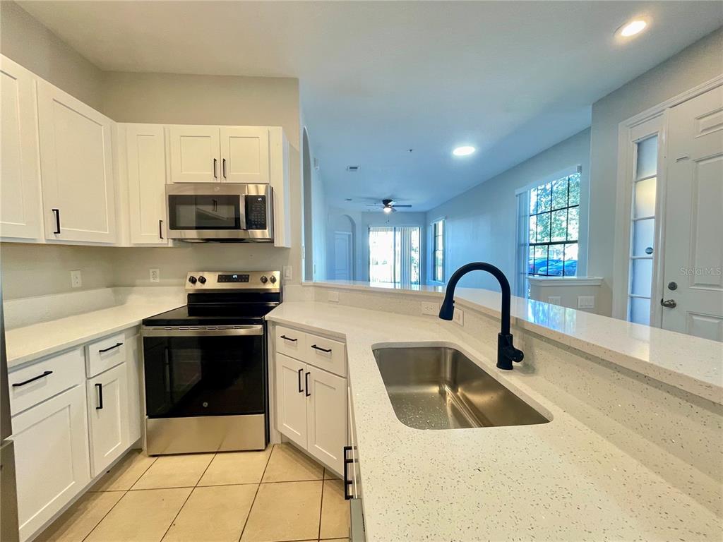 A kitchen features white cabinets, stainless steel appliances, and a quartz countertop with a sink — 2944 OAK PARK WAY UNIT 1453, ORLANDO, FL