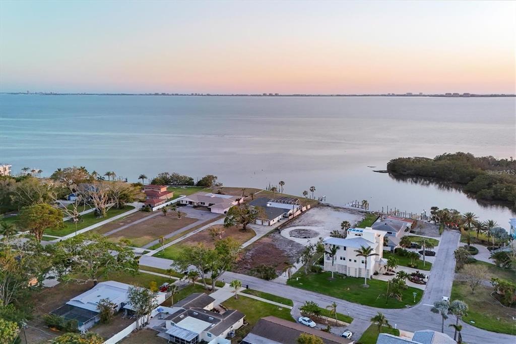 An aerial view shows waterfront houses and vacant lots along a bay at sunset — 7318 WESTMORELAND DRIVE, SARASOTA, FL