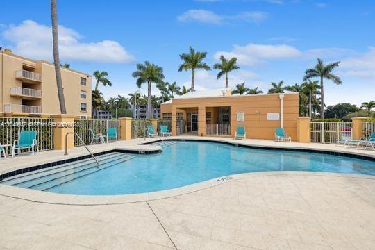 An outdoor swimming pool surrounded by a patio, lounge chairs, palm trees, and apartment buildings — DANIA BEACH, FL