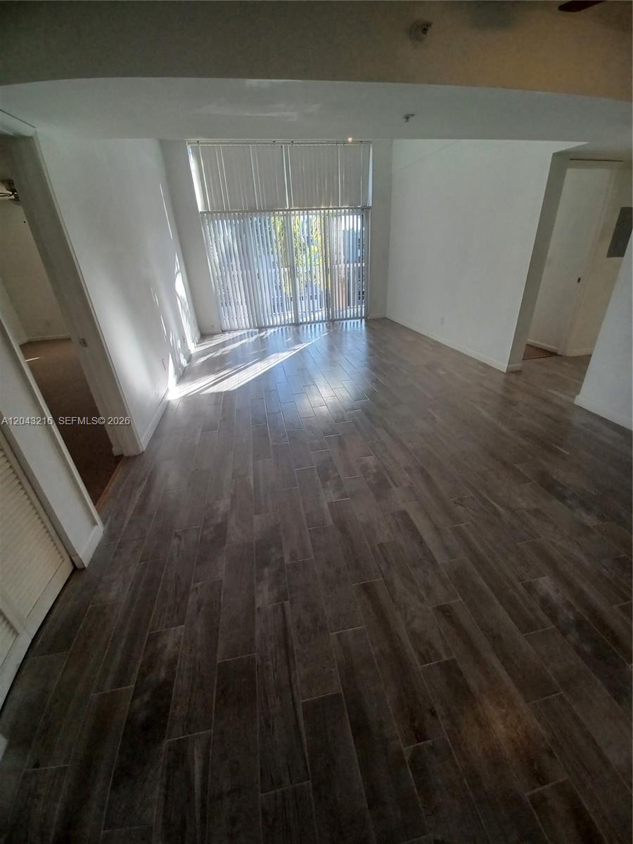 An empty room features wood-look tile flooring, white walls, and floor-to-ceiling vertical blinds — DANIA BEACH, FL
