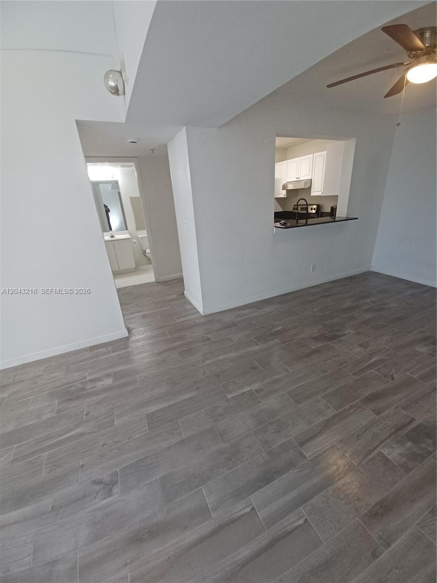 A living area with gray wood-look tile flooring leads to a kitchen pass-through and bathroom — DANIA BEACH, FL