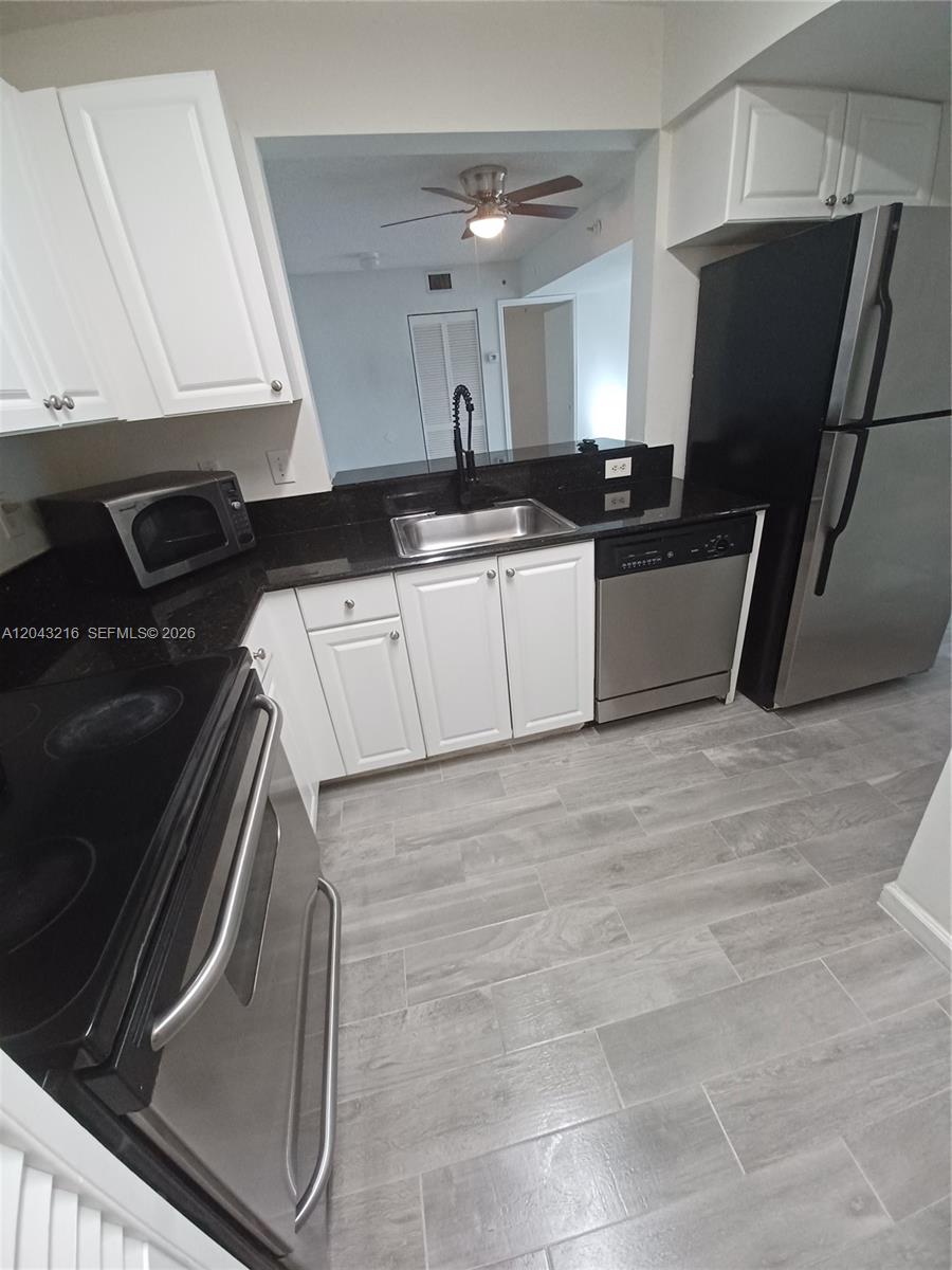 A kitchen features white cabinets, black countertops, stainless steel appliances, and gray wood-look tile flooring — DANIA BEACH, FL