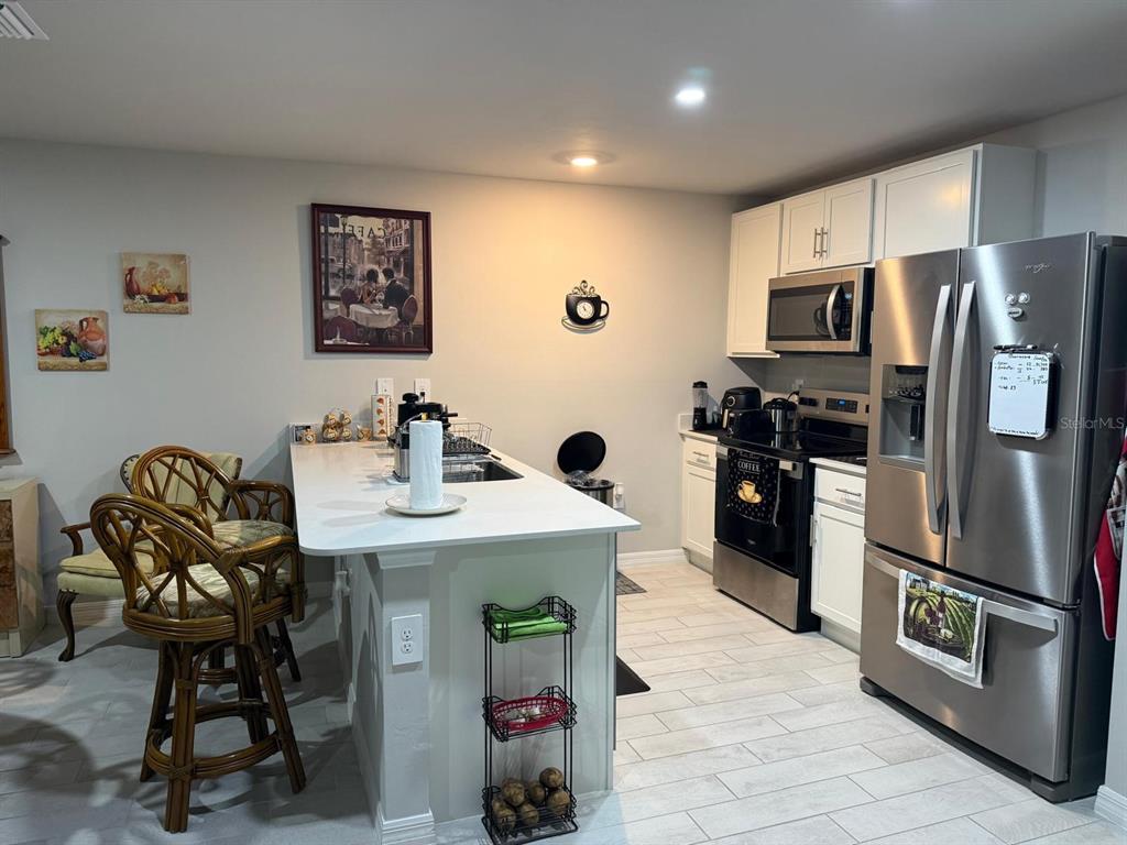 A kitchen features white cabinets, stainless steel appliances, a center island, and wicker bar stools — 1580 BISCAYNE DRIVE, PORT CHARLOTTE, FL