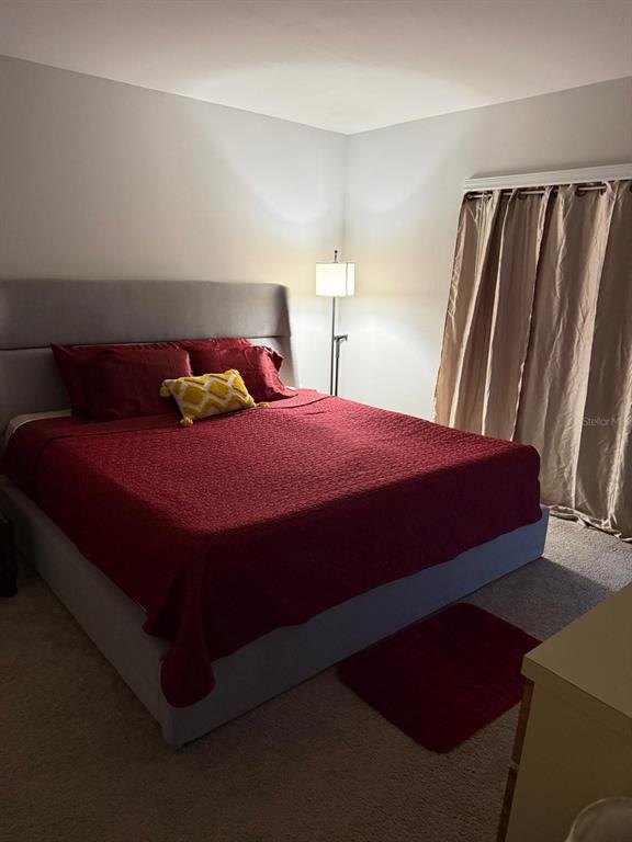 A bedroom features a gray upholstered bed with a red quilt and a floor lamp — 1580 BISCAYNE DRIVE, PORT CHARLOTTE, FL