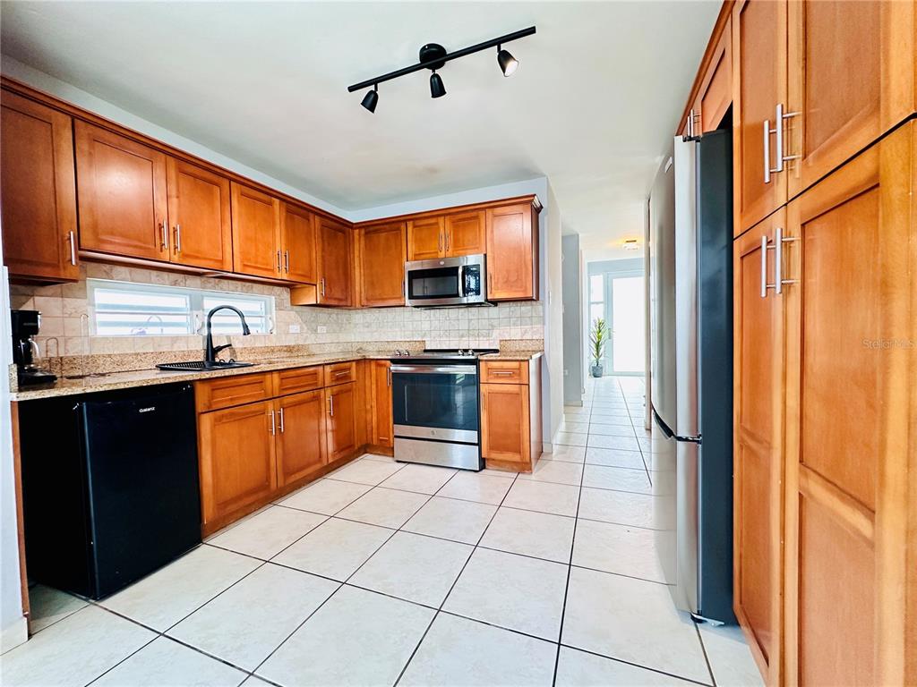 A kitchen features wood cabinets, stainless steel appliances, granite countertops, and light-colored tile flooring — Calle Isleña HACIENDA PALOMA, LUQUILLO, PR