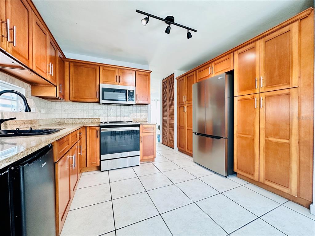 A kitchen with wood cabinets, stainless steel appliances, granite countertops, and light-colored tile flooring — Calle Isleña HACIENDA PALOMA, LUQUILLO, PR