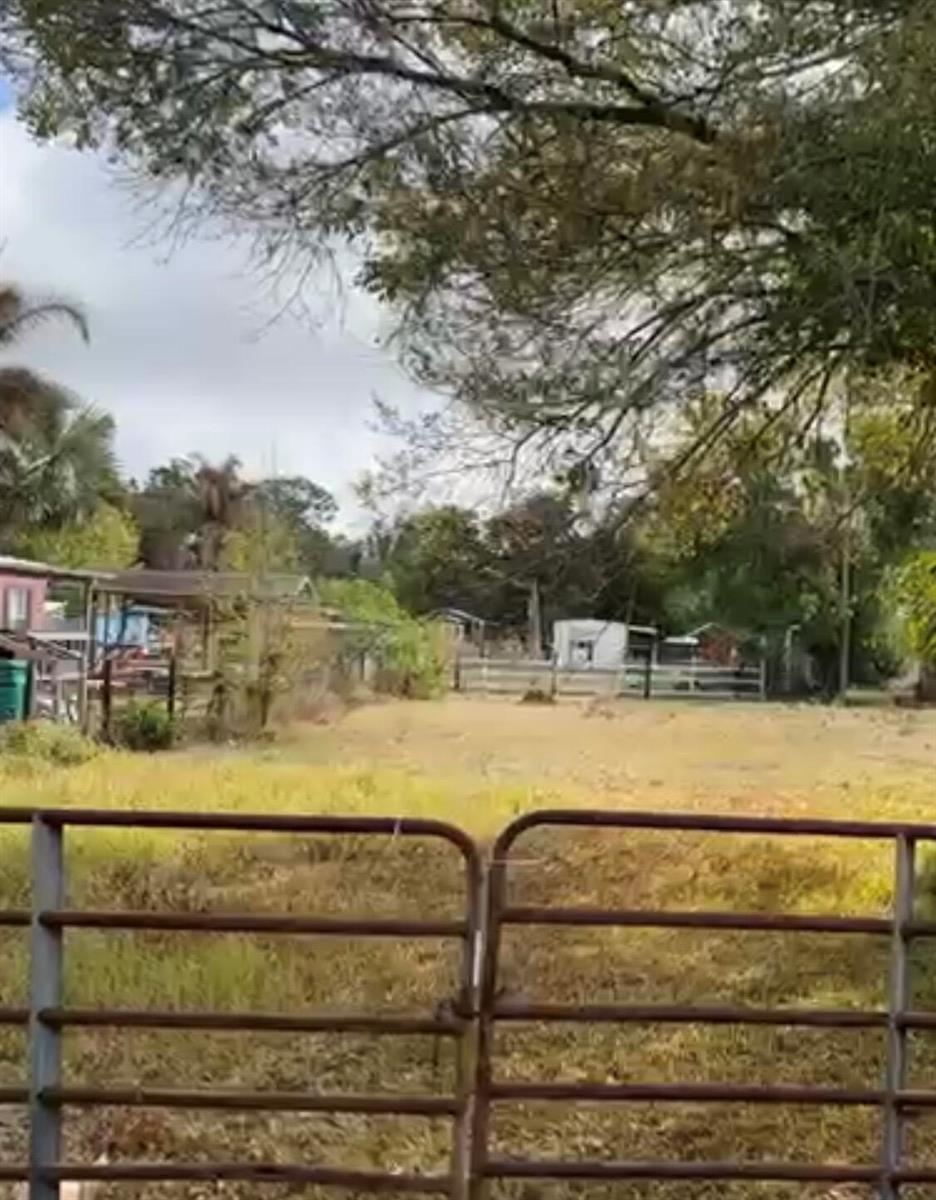 A view of a grassy lot with a metal gate in the foreground and structures — 854 NE 42nd Terrace, Okeechobee FL 34972, OKEECHOBEE, FL