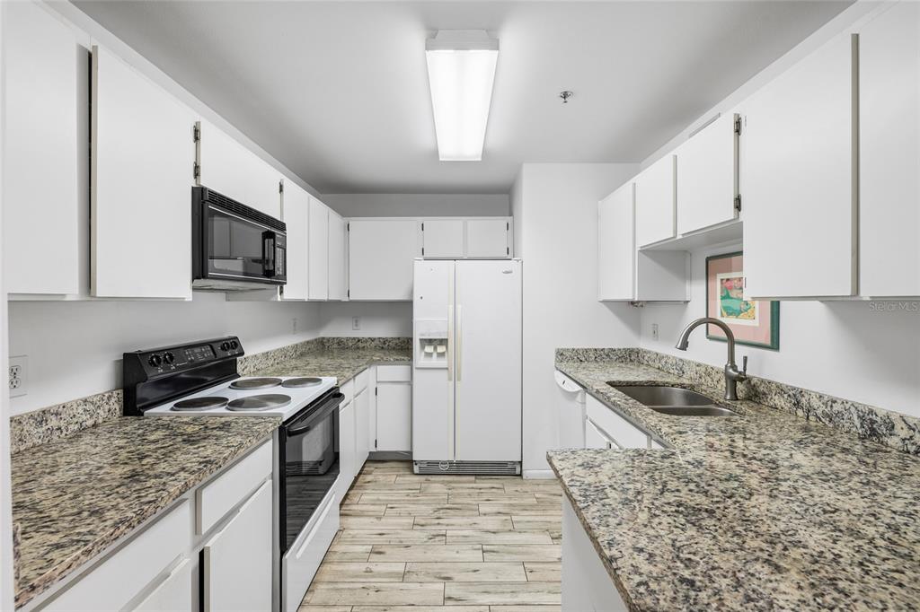 A galley kitchen features white cabinets, granite countertops, stainless steel appliances, and wood-look tile flooring — 3002 W CLEVELAND STREET UNIT B6, TAMPA, FL