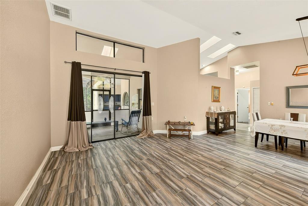 A living area with wood-look tile flooring, high ceilings, and sliding glass doors to a patio — 9757 HERMOSILLO DRIVE, NEW PORT RICHEY, FL