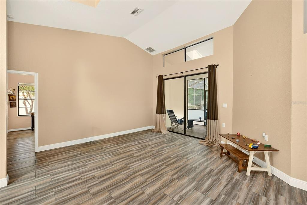A living room with vaulted ceilings, wood-look tile flooring, and sliding glass doors to a lanai — 9757 HERMOSILLO DRIVE, NEW PORT RICHEY, FL