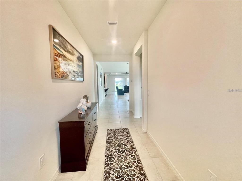 A long hallway with tile flooring leads to an open living area with a runner — 14311 59TH CIRCLE E, BRADENTON, FL