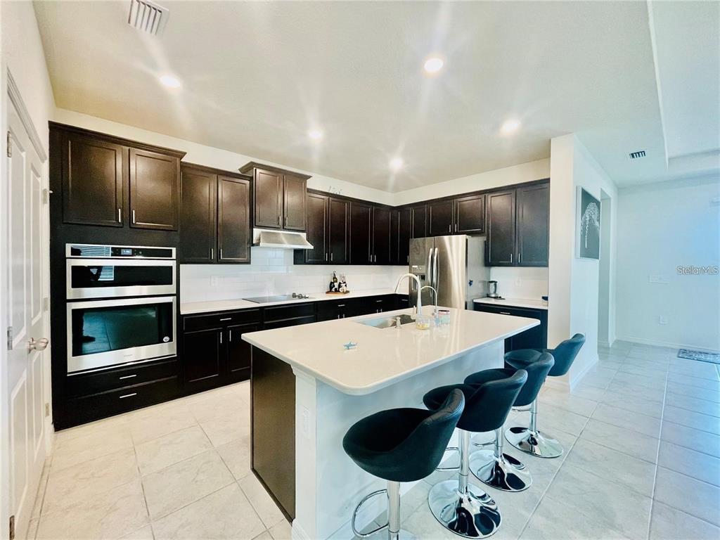 A kitchen features dark cabinetry, white countertops, a central island, and stainless steel appliances — 14311 59TH CIRCLE E, BRADENTON, FL