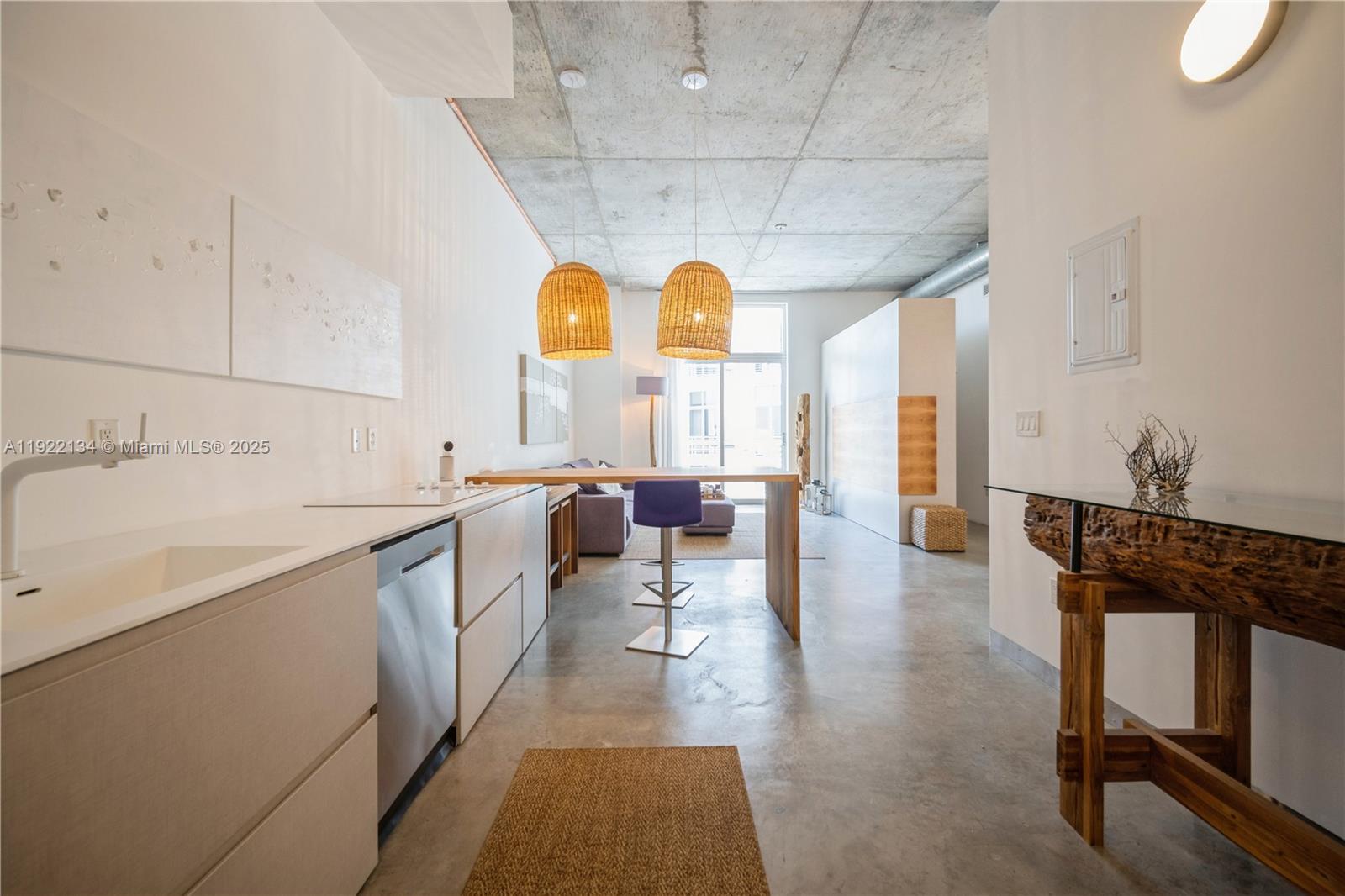 A modern open-concept kitchen and living area features concrete ceilings, light cabinetry, and woven pendants — 2001 Meridian Ave # 512, Miami Beach FL 33139, MIAMI BEACH, FL
