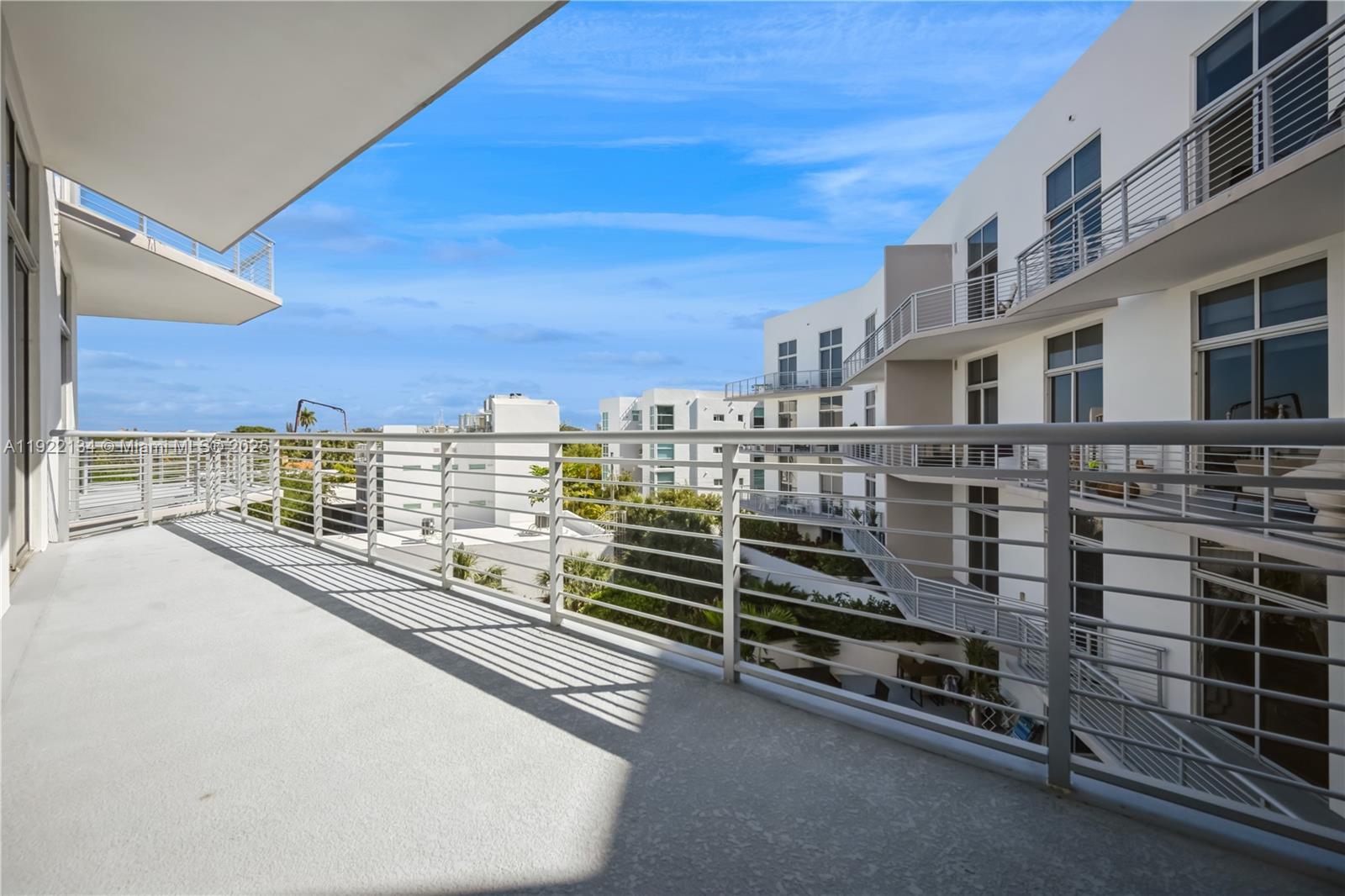A spacious balcony with metal railings overlooks a courtyard between modern white apartment buildings — 2001 Meridian Ave # 512, Miami Beach FL 33139, MIAMI BEACH, FL