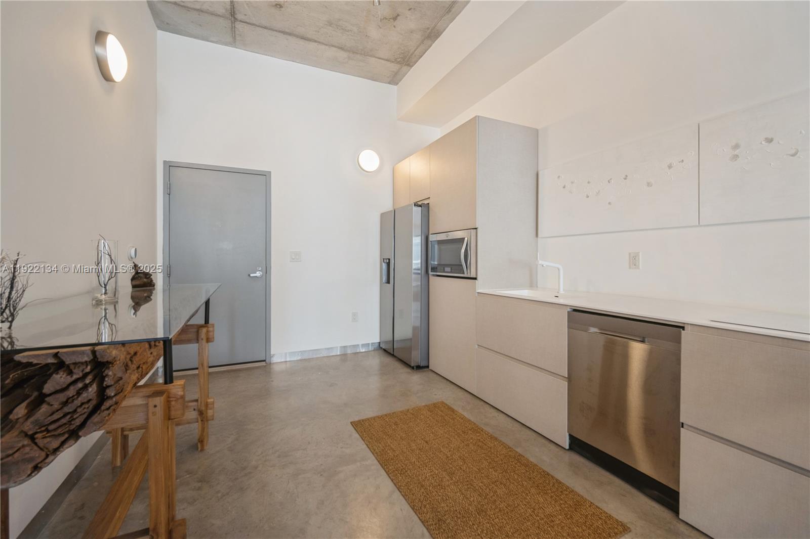 A modern kitchen features concrete ceilings, stainless steel appliances, and a rustic wood-accented table — 2001 Meridian Ave # 512, Miami Beach FL 33139, MIAMI BEACH, FL