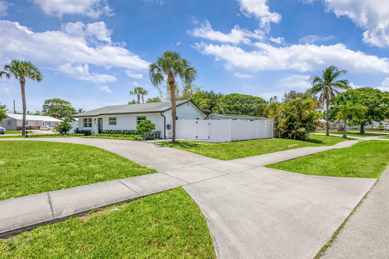 A white single-story house features a curved driveway, a white vinyl fence, and palm trees — 204 W Whitney Drive, Jupiter FL 33458, JUPITER, FL