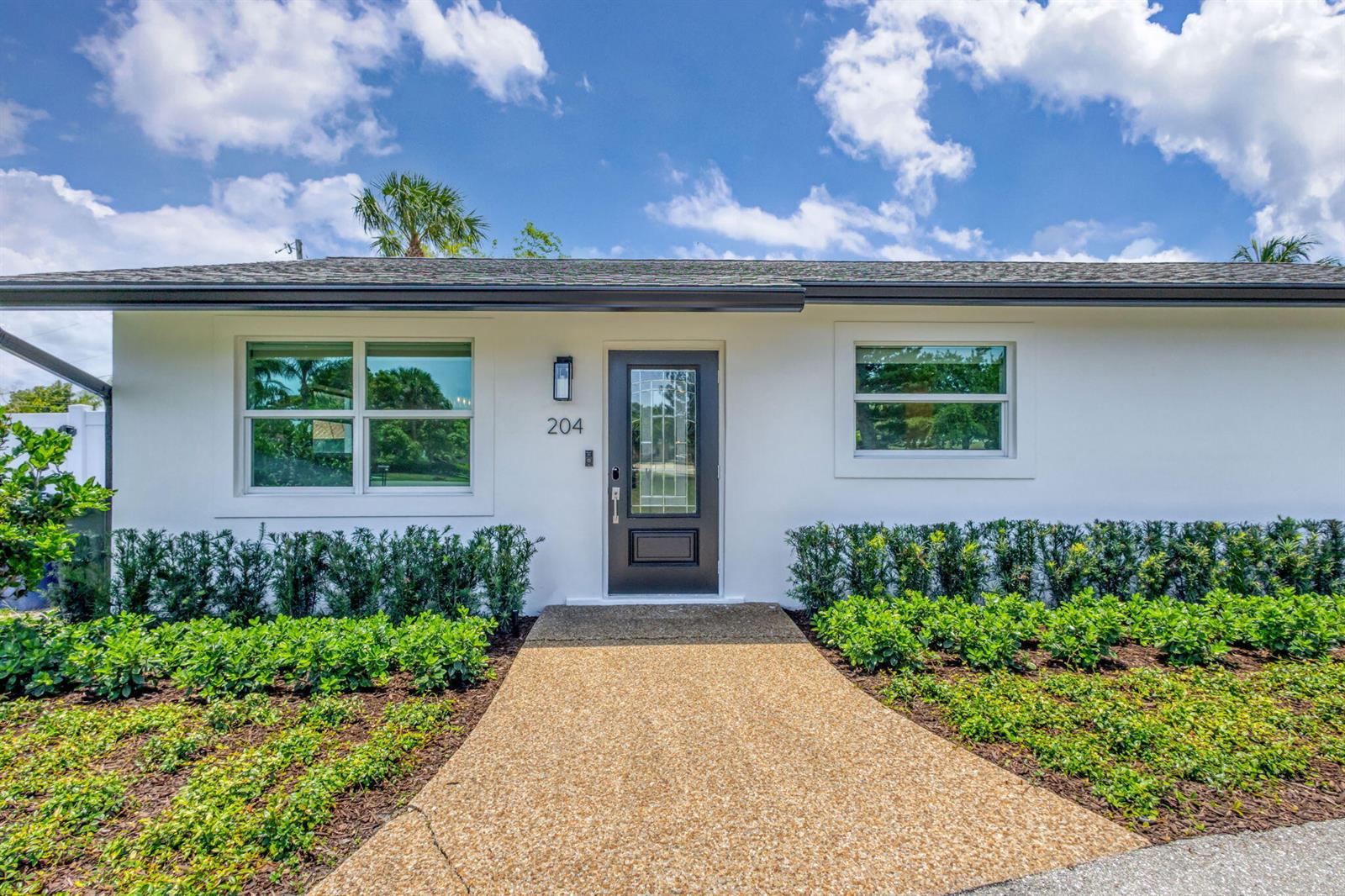 A white house exterior features a dark front door, a walkway, and manicured green hedges — 204 W Whitney Drive, Jupiter FL 33458, JUPITER, FL