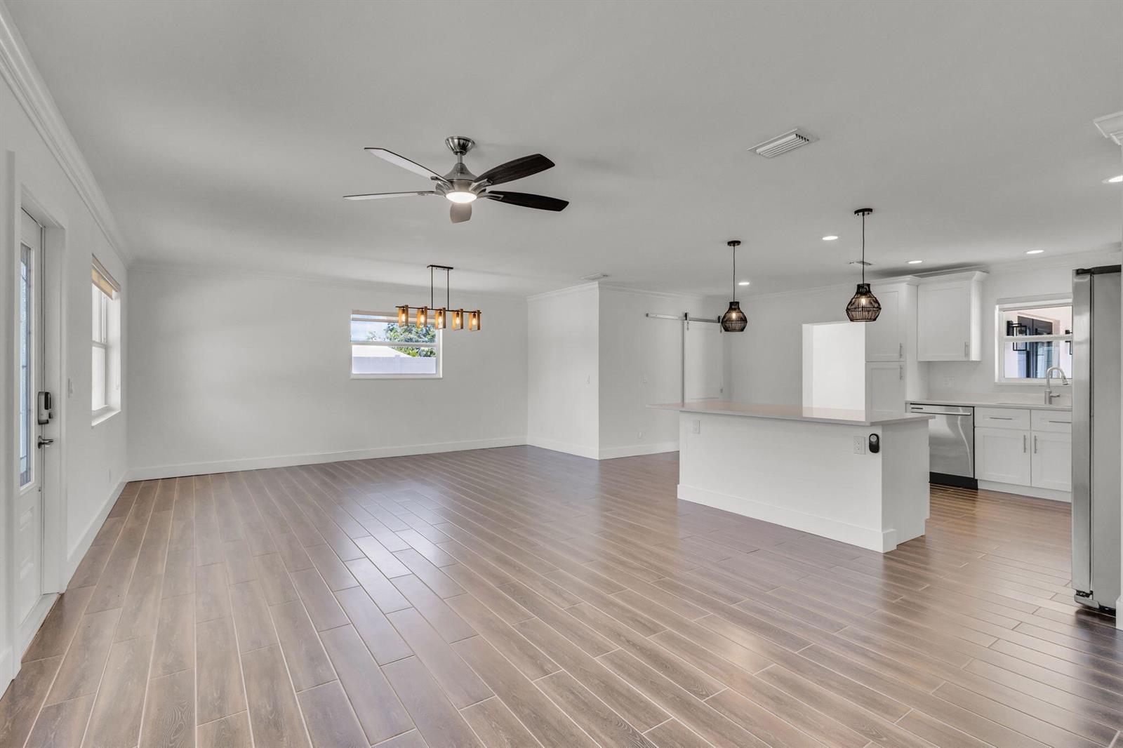An open-concept kitchen and living area features white cabinetry, wood-look tile flooring, and pendant lighting — 204 W Whitney Drive, Jupiter FL 33458, JUPITER, FL