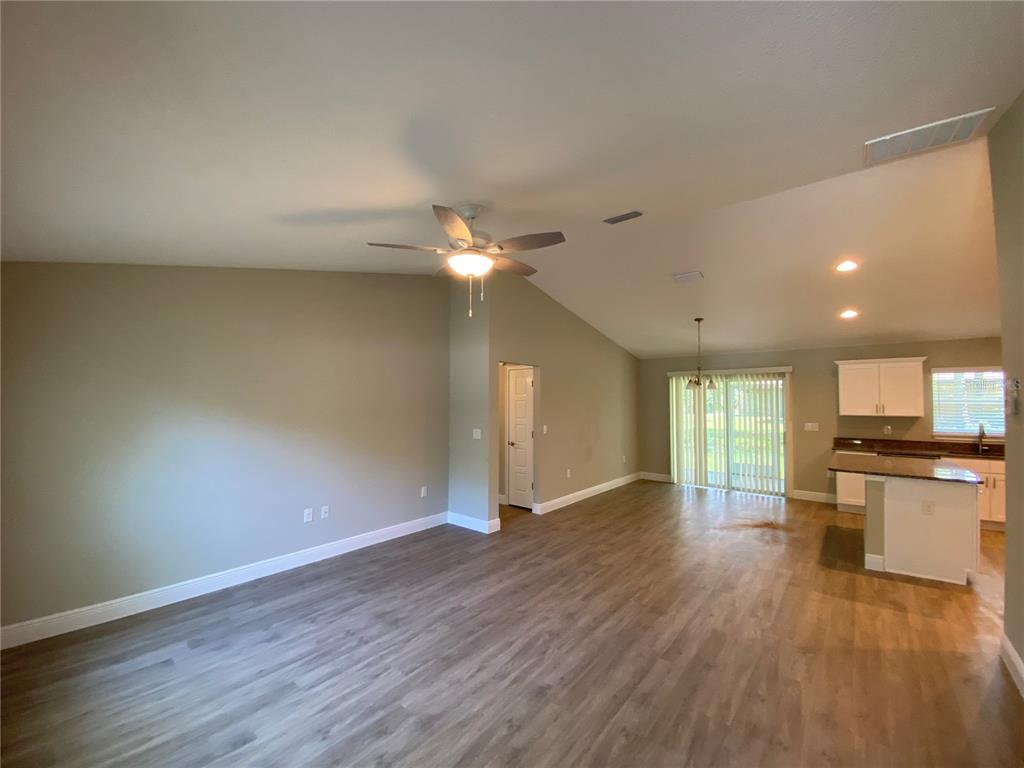 An open-concept living room with vaulted ceilings, wood-look flooring, and an adjacent kitchen area — 12 OAK TRAIL, OCALA, FL