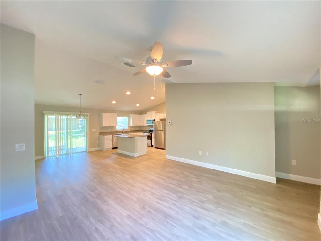 An open-concept living area features light wood-look flooring, a ceiling fan, and a kitchen — 12 OAK TRAIL, OCALA, FL