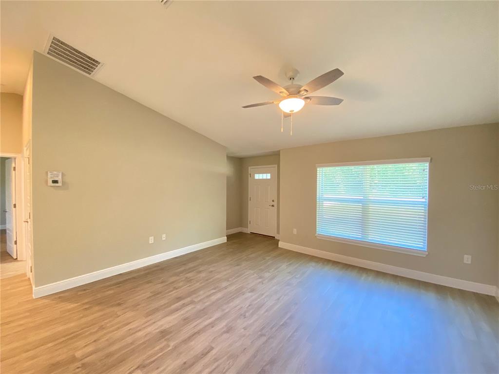 A living room features light-colored walls, wood-look flooring, a ceiling fan, and a large window — 12 OAK TRAIL, OCALA, FL