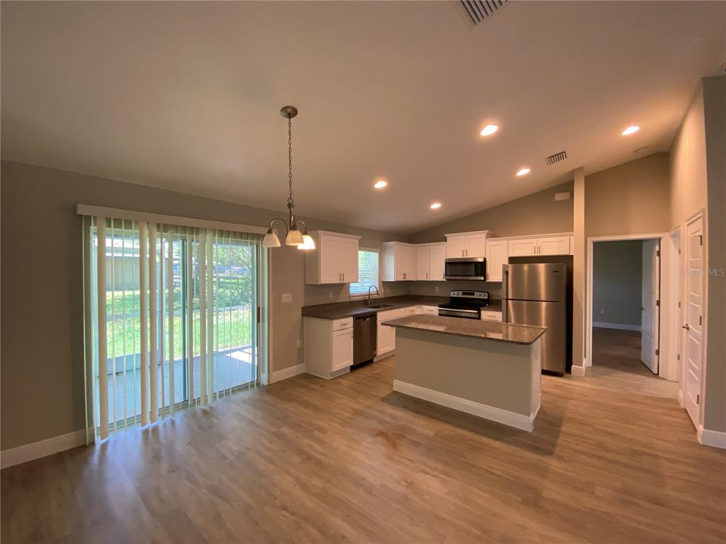 A kitchen with white cabinets, stainless steel appliances, and an island opens to a dining area — 12 OAK TRAIL, OCALA, FL