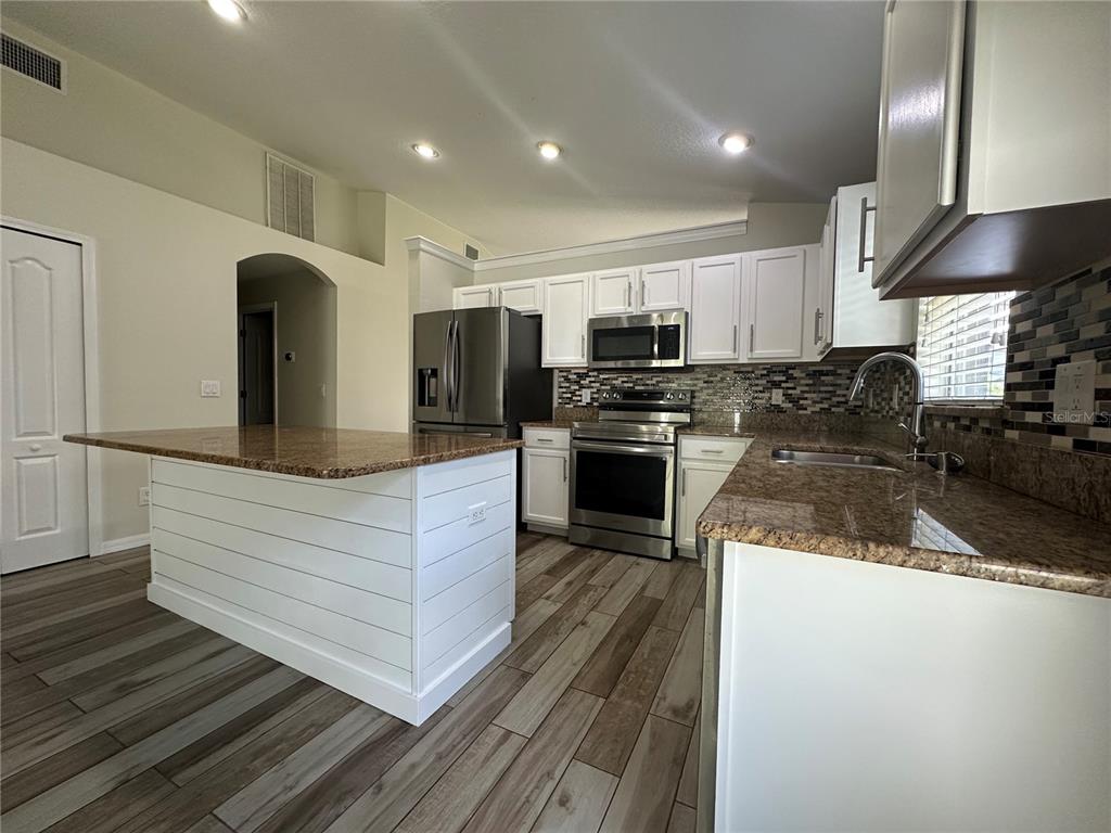 A kitchen features white cabinets, granite countertops, stainless steel appliances, and a white shiplap island — 3145 DUNSTABLE DRIVE, LAND O LAKES, FL
