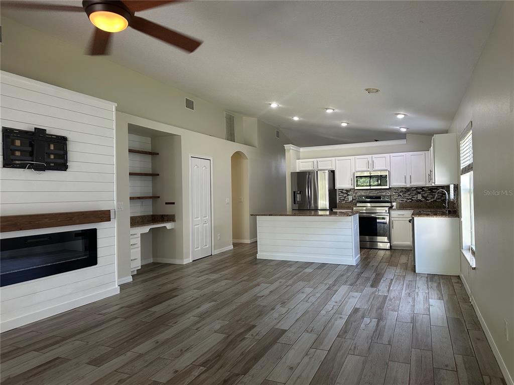 An open-concept living area features a fireplace, built-in shelving, and a kitchen with white cabinets — 3145 DUNSTABLE DRIVE, LAND O LAKES, FL