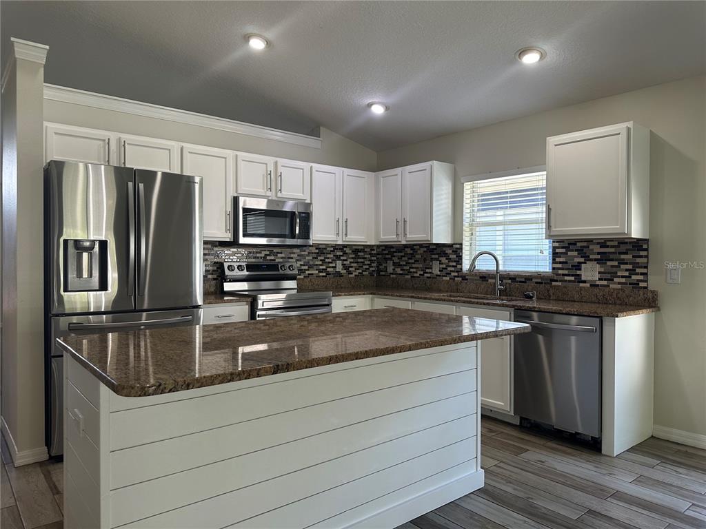 A kitchen features white cabinets, granite countertops, stainless steel appliances, and a shiplap-sided island — 3145 DUNSTABLE DRIVE, LAND O LAKES, FL